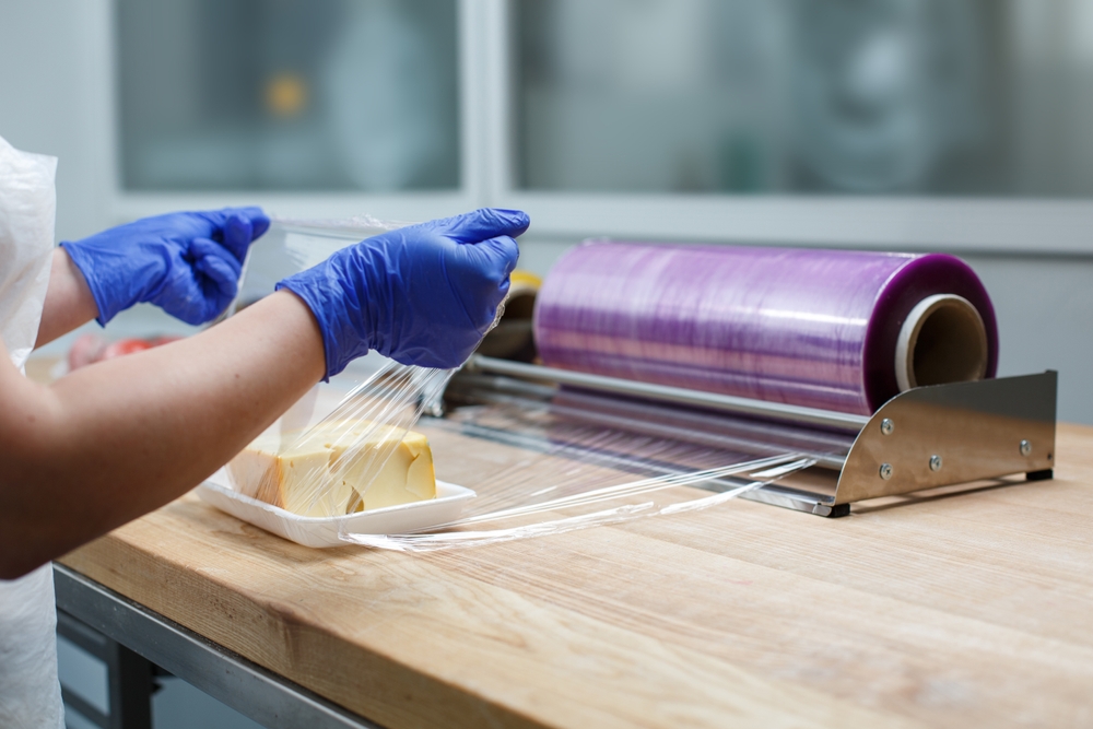 Worker,Wraps,Tray,With,Piece,Of,Cheese,With,Cling,Film,